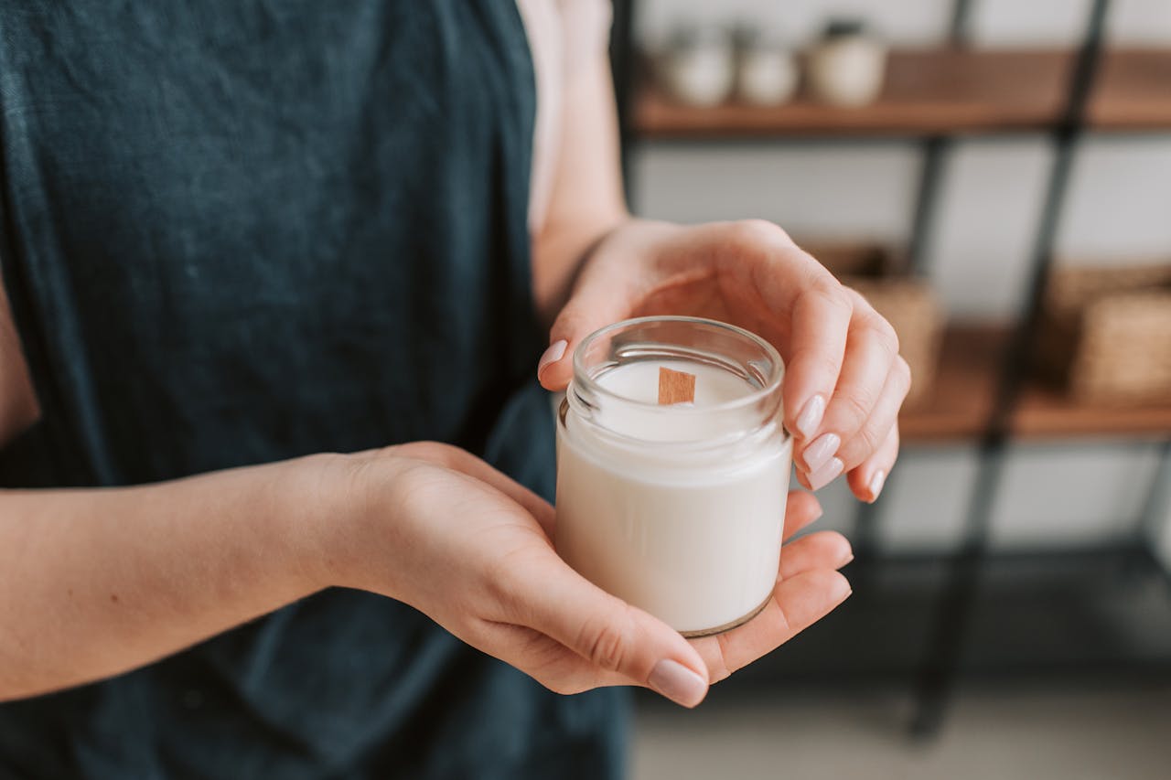 Close-up of hands holding a jar candle indoors on a softly focused background.